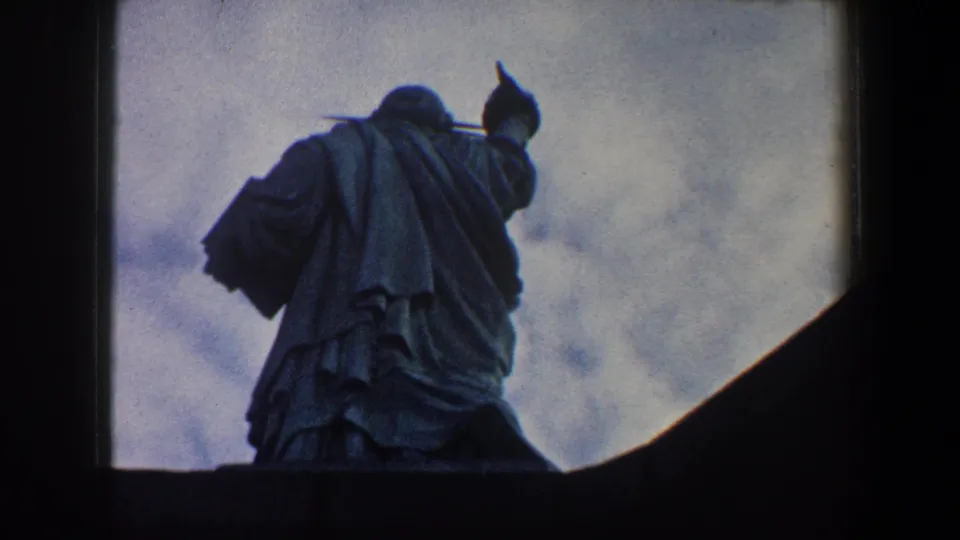 New York City home-movie frame from 1960 showing the Statue of Liberty from behind, silhouetted beside a dark foreground shape.