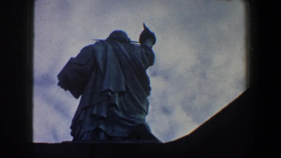 1960 New York City 8mm frame showing the Statue of Liberty from below, silhouetted against a cloudy sky.