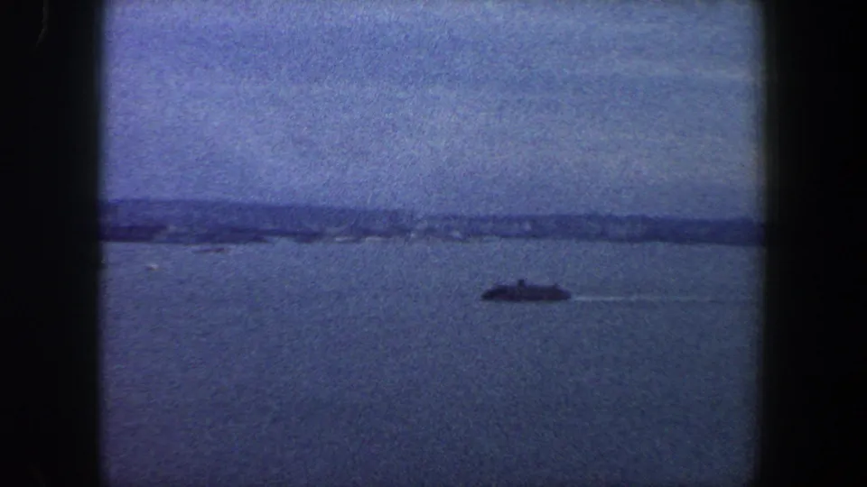 Wide 1960 New York City harbor frame showing a ship or ferry on the water and a soft distant shoreline.
