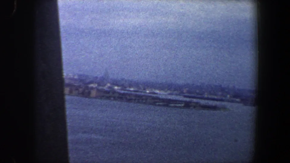 Soft, blue-tinted 1960 New York City waterfront view with open harbor water and distant shoreline structures.
