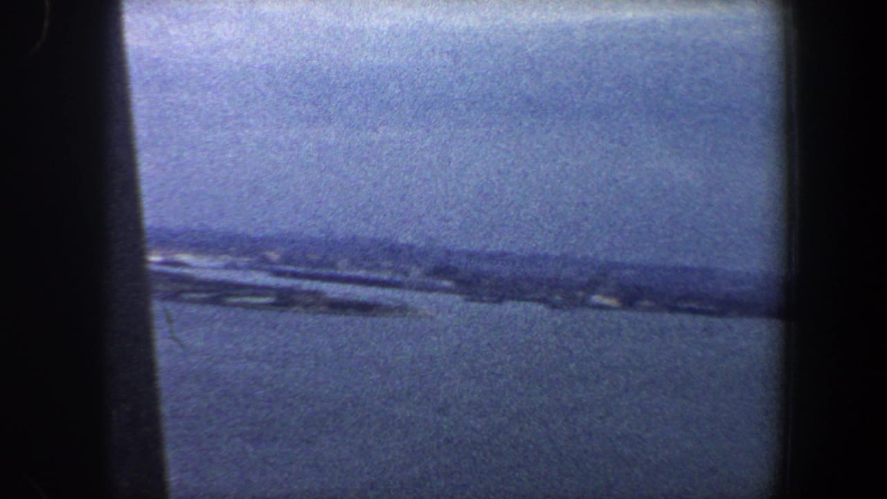 Blue water and a hazy distant shoreline seen through dark film-frame edges.