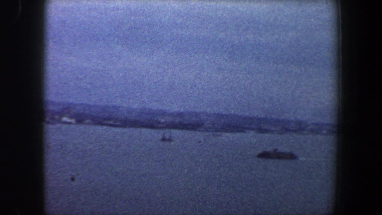 Distant shoreline across blue water with a small dark boat at right.