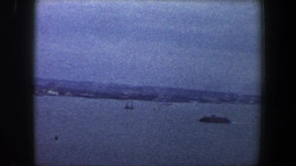 1960 8mm view across New York City-area water toward a hazy shoreline, with a small dark boat visible on the right.