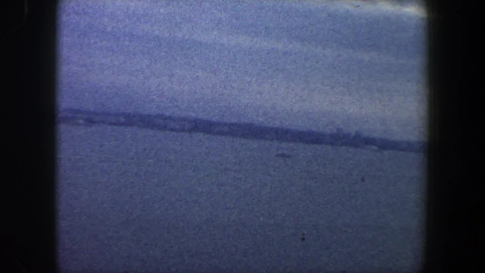1960 8mm coastal view in New York City, showing open blue water, a faint shoreline, and visible dark film gate borders.