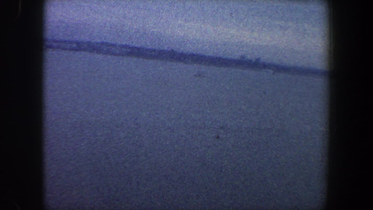 1960 archival 8mm frame from New York City metadata showing a muted water horizon beneath an overcast sky.