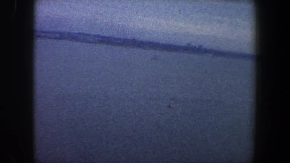 1960 archival 8mm frame from New York City metadata showing a muted water horizon beneath an overcast sky.