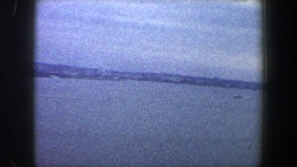 Archival 8mm view of a calm body of water and cloudy sky, with a distant dark shoreline-like band across the frame.