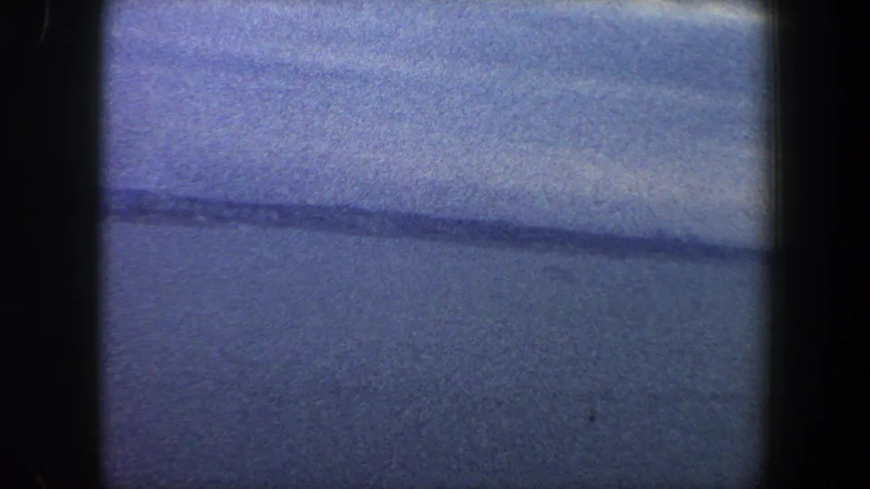 1960 New York City metadata frame showing a cool-toned water horizon under cloud cover, with soft 8mm grain and exposure variation.