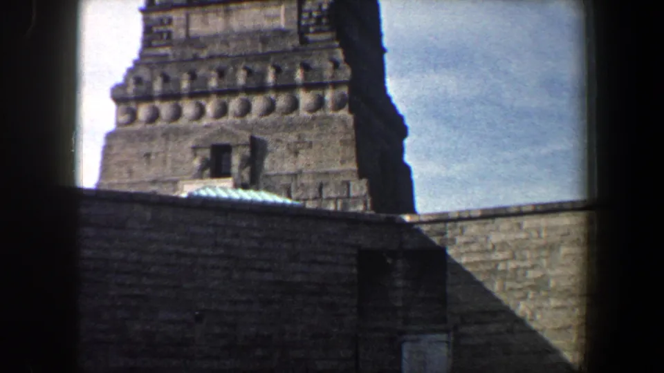 1960s New York City 8mm frame showing a historic stone tower, masonry wall, small openings, and blue sky.