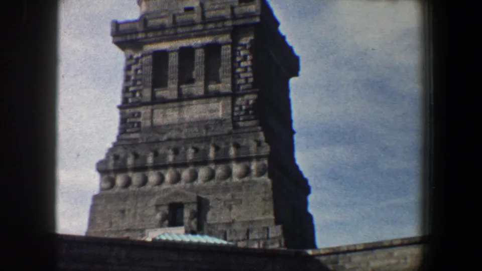 1960s New York City 8mm frame of a stone landmark tower with arched openings, patterned masonry, wall, and sky.