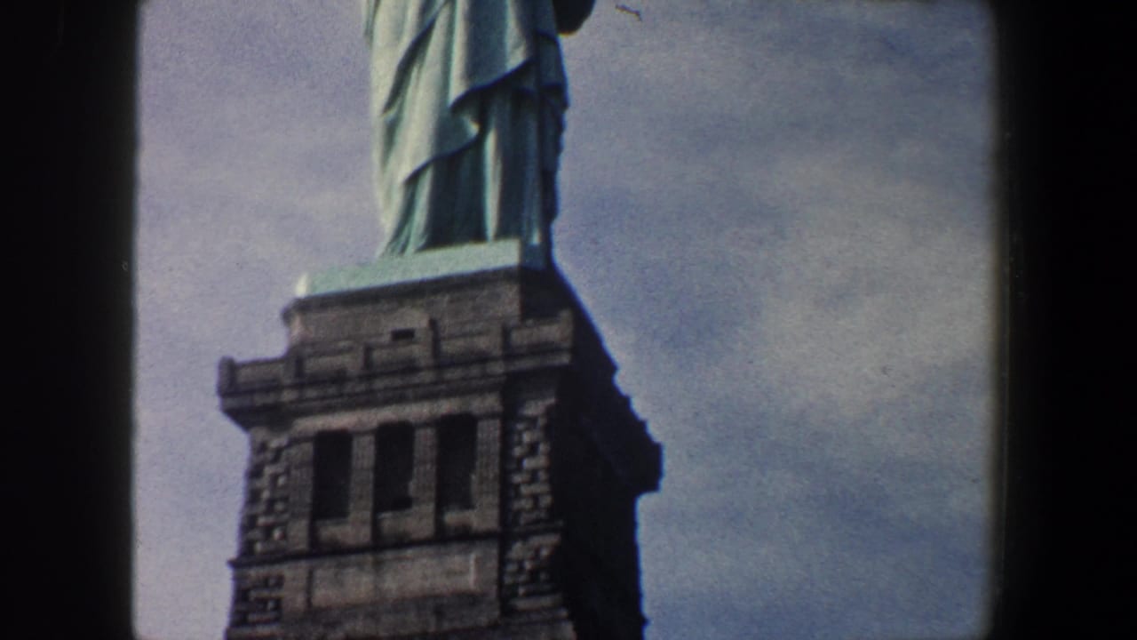 1960 New York City home-movie frame showing the upper stone pedestal and lower section of the Statue of Liberty during an upward tilt.