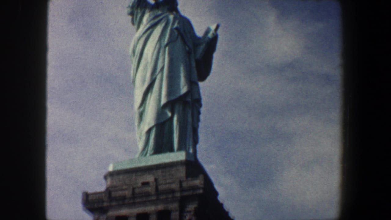 1960 New York City 8mm frame showing the Statue of Liberty from below, with the upper pedestal and cloudy sky visible.