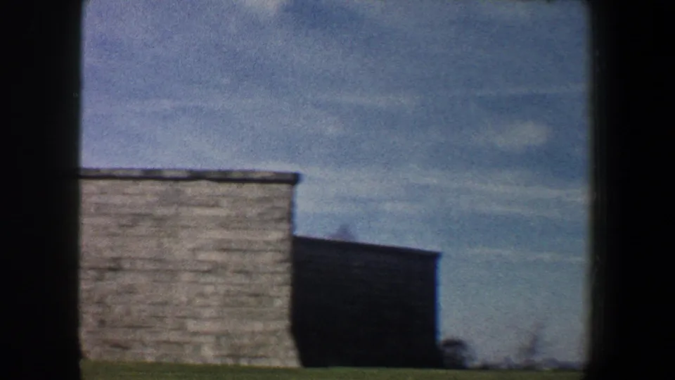 1960 New York City 8mm frame with the pedestal edge, stone wall, and cloudy sky after the camera tilts down.
