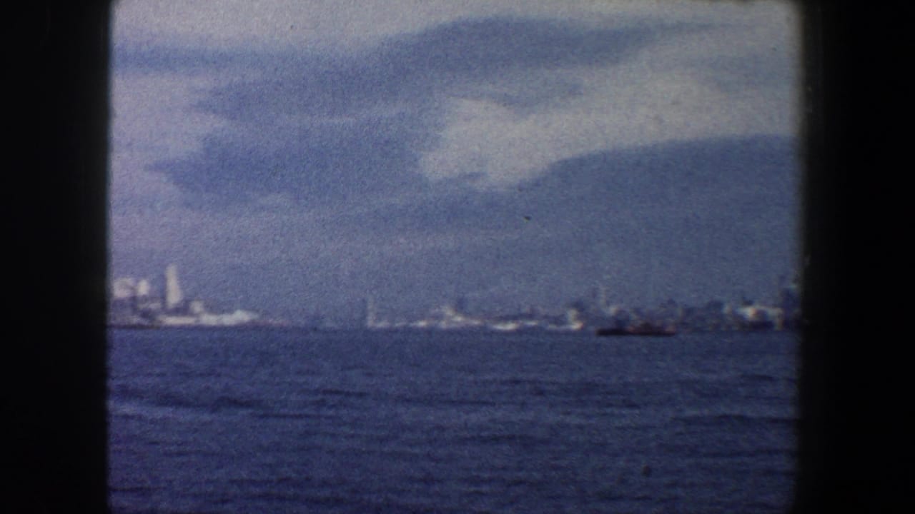 Wide blue-water view with distant shoreline, skyline shapes, and a small boat at right.