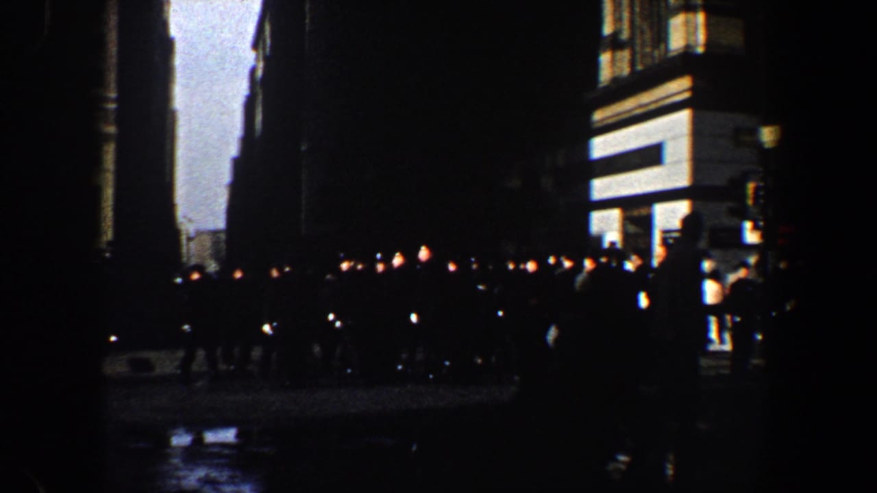 1960 New York City home-movie frame showing pedestrians silhouetted on a wet nighttime street beside lit building facades.