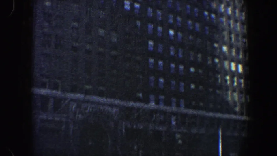 Handheld 8mm view of a New York City high-rise facade with many windows, dark exposure, and faint street-level details.