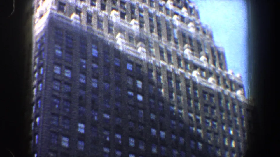 1960 New York City upward street view showing a tall masonry high-rise, window rows, bright sky, and dark film border.