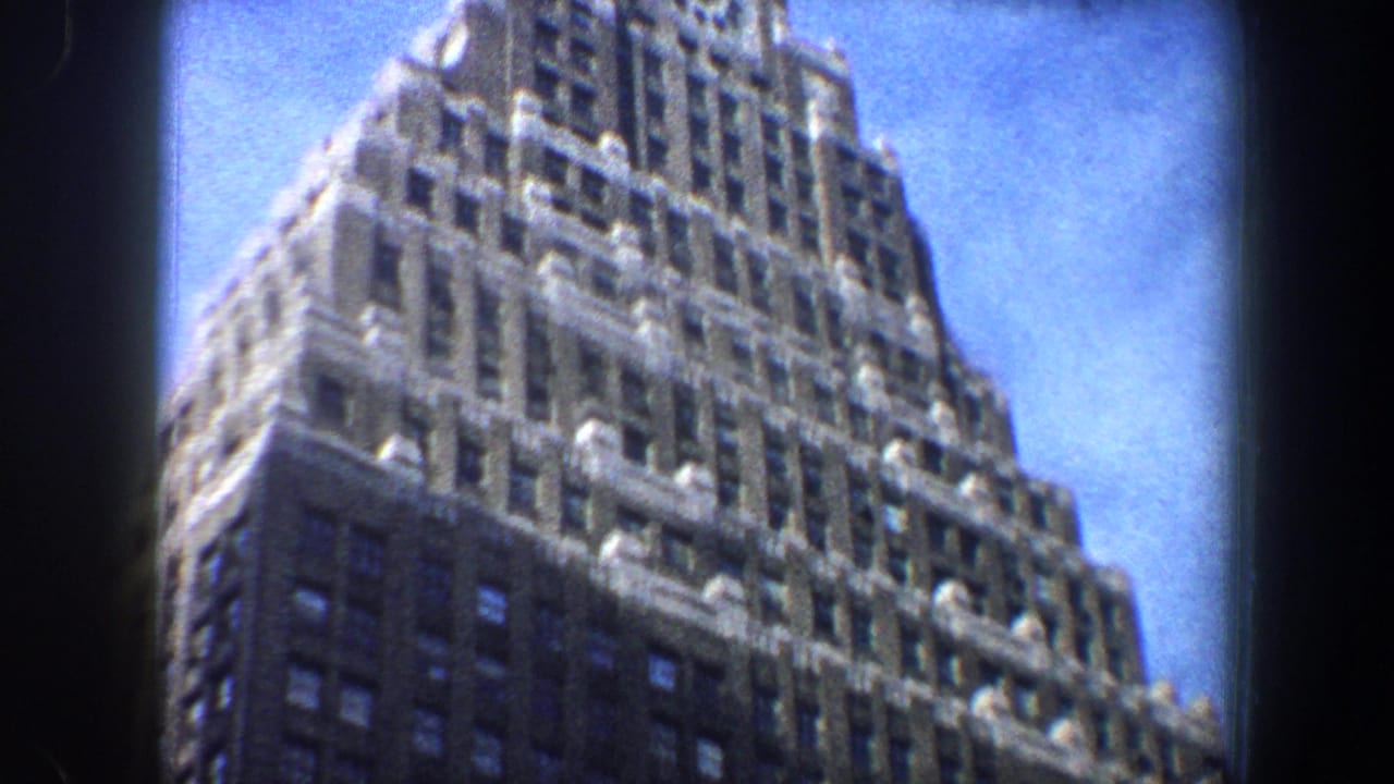 1960 New York City 8mm frame showing a low-angle view of a tall Art Deco-style skyscraper with a stepped facade.