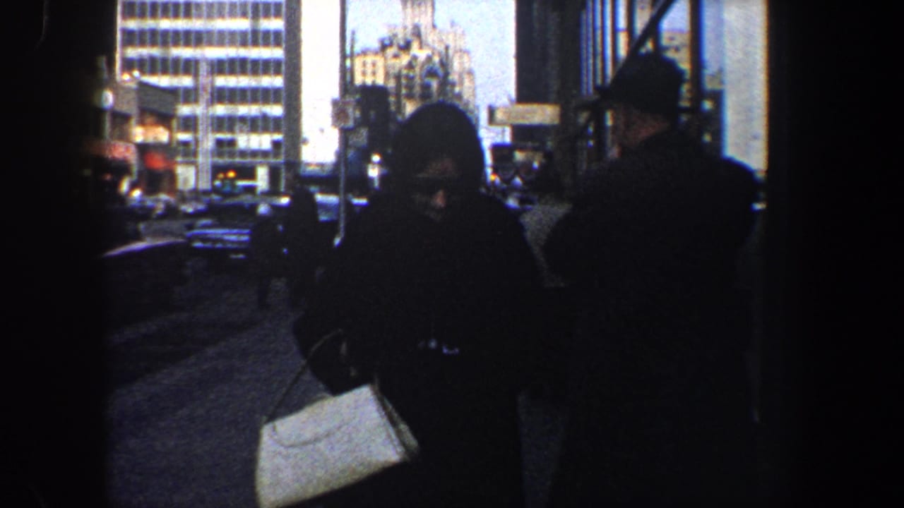Sidewalk scene with pedestrians in dark coats and a woman carrying a light handbag.