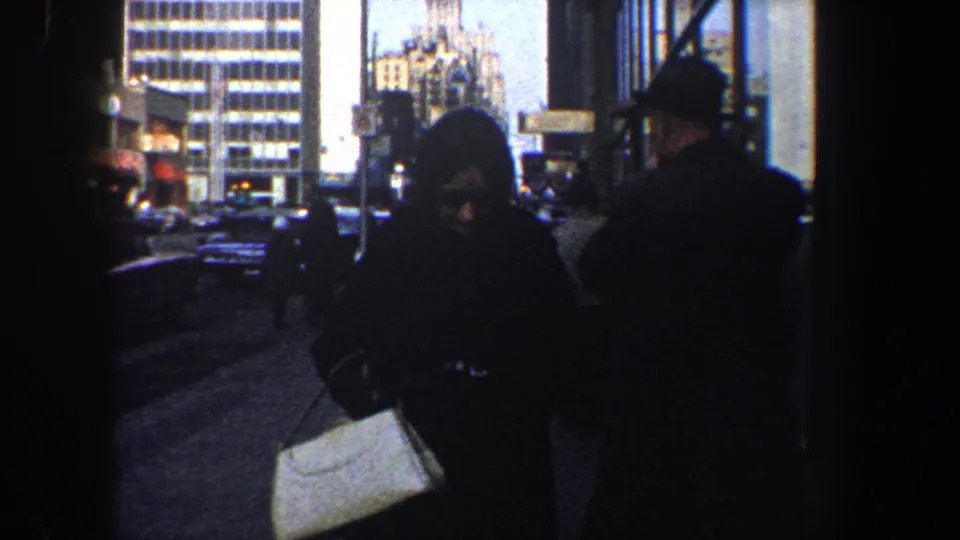 New York City sidewalk scene with pedestrians in coats moving past storefront shadows and mid-century buildings.