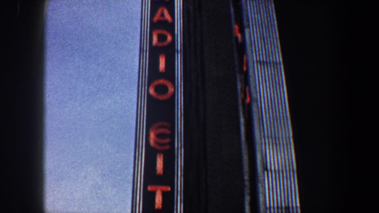 1960 New York City view of the Radio City vertical neon sign rising beside a dark Art Deco facade.