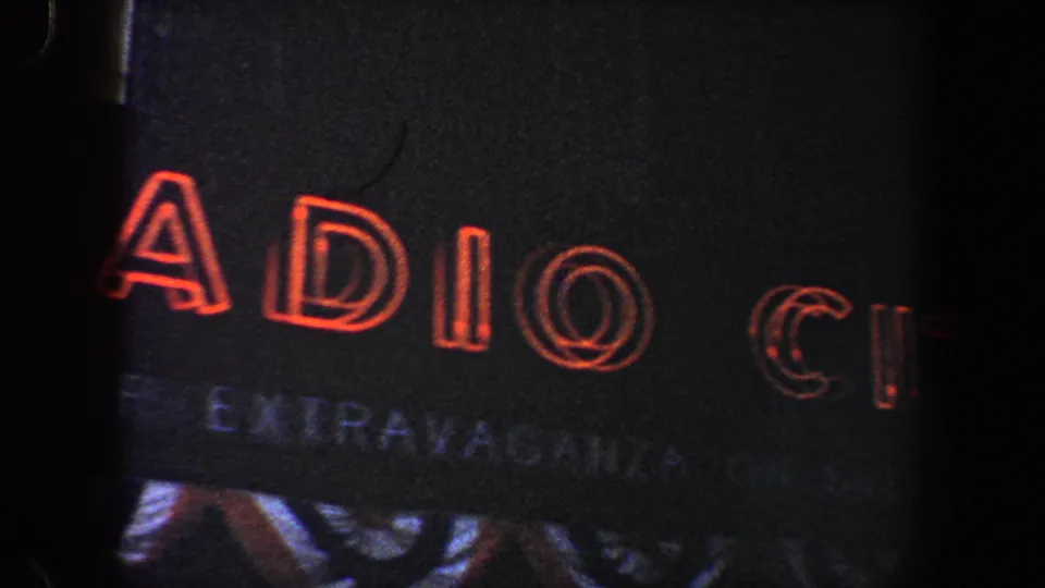 Close 8mm frame of red Radio City lettering on the dark sign surface, with partial smaller text below.