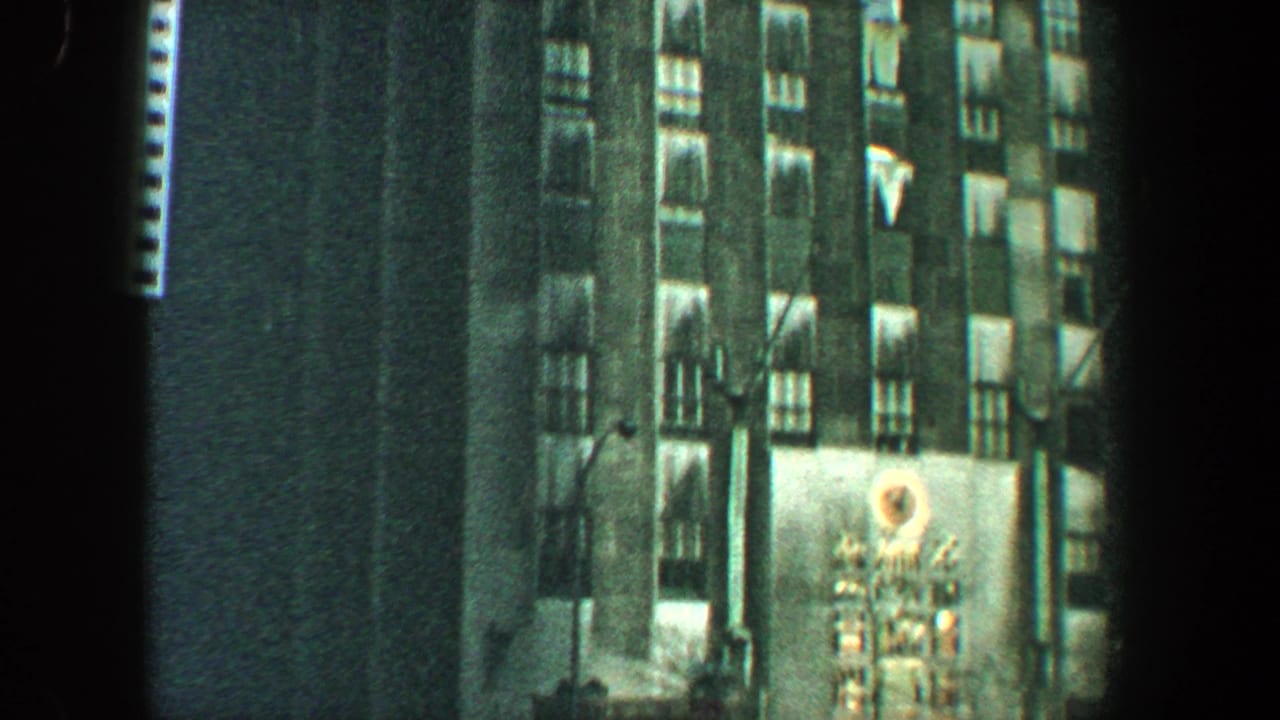 Tall building facade at night with lit windows and a circular sign.