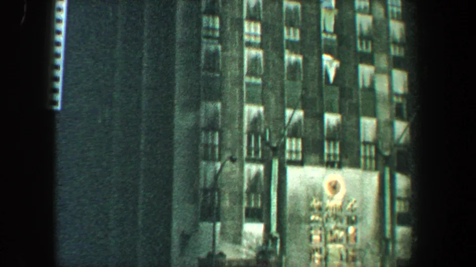 Night view of a New York City high-rise facade with lit windows and a circular commercial display visible near the lower right.