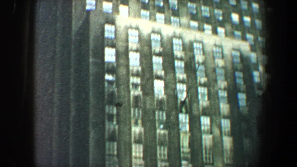 1960 New York City home-movie frame showing a tall building facade with many bright window rows and soft handheld blur.