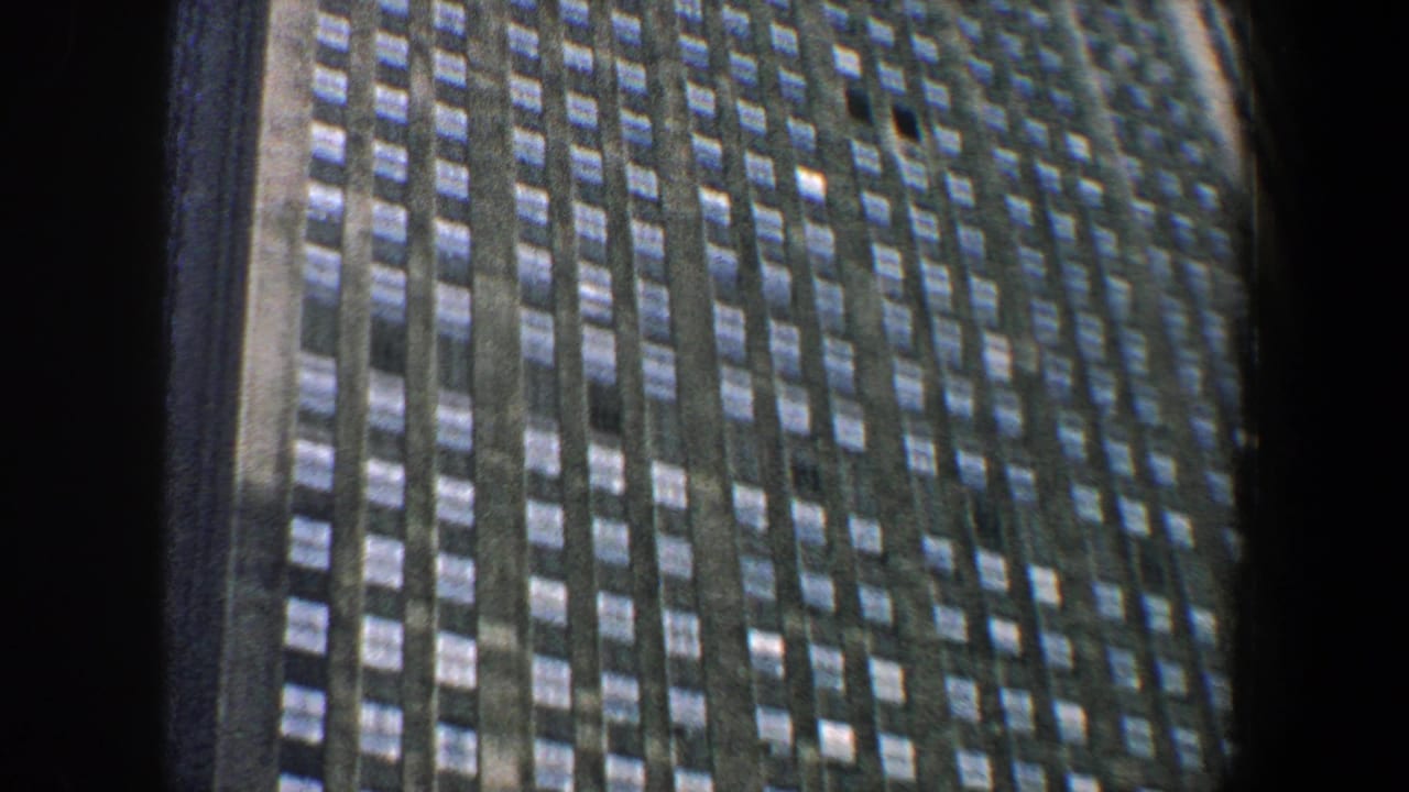1960 New York City 8mm frame showing a tall business building facade viewed from below, with repeated windows and dark film borders.