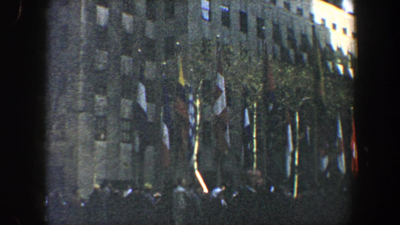 Crowd gathered below a large building lined with international flags.