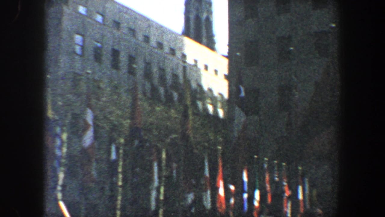 Flag-lined building facade with a crowd partly visible below.