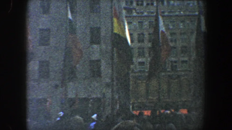 Final 8mm frame showing people at the bottom of a New York City building facade with flags rising through the scene.