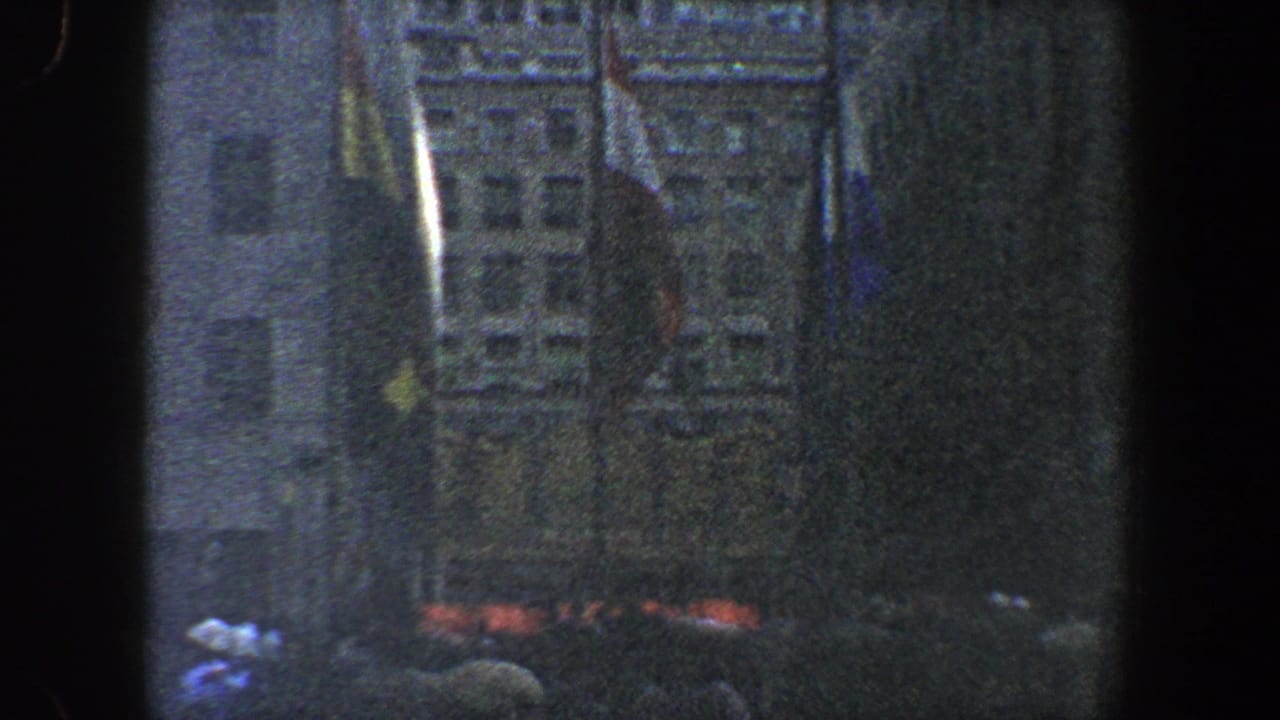 Dark nighttime crowd in front of tall buildings with flags visible above the gathering.