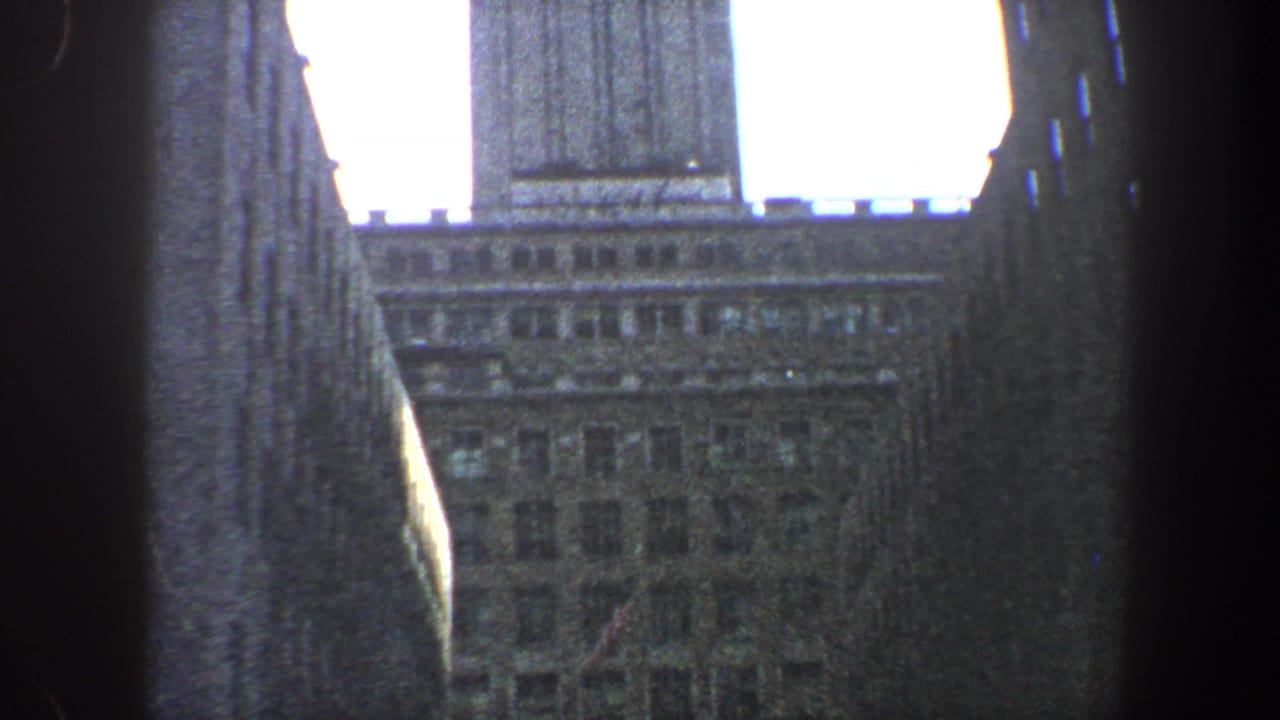 Upward view of a high-rise roofline and surrounding buildings against bright sky.