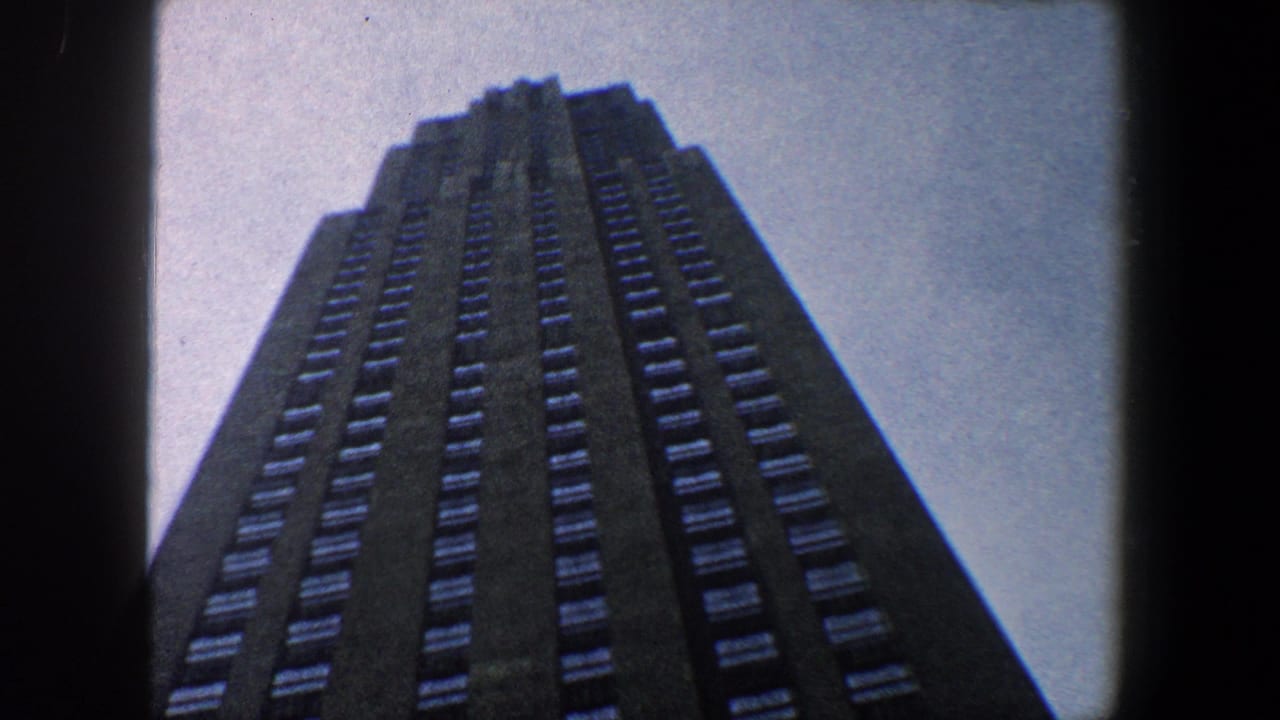 Low-angle view of a dark skyscraper rising into pale sky.