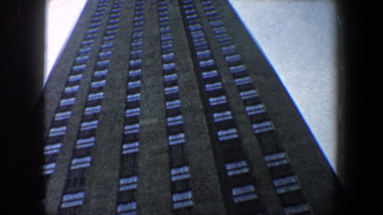Tall dark building facade seen from below against bright sky.