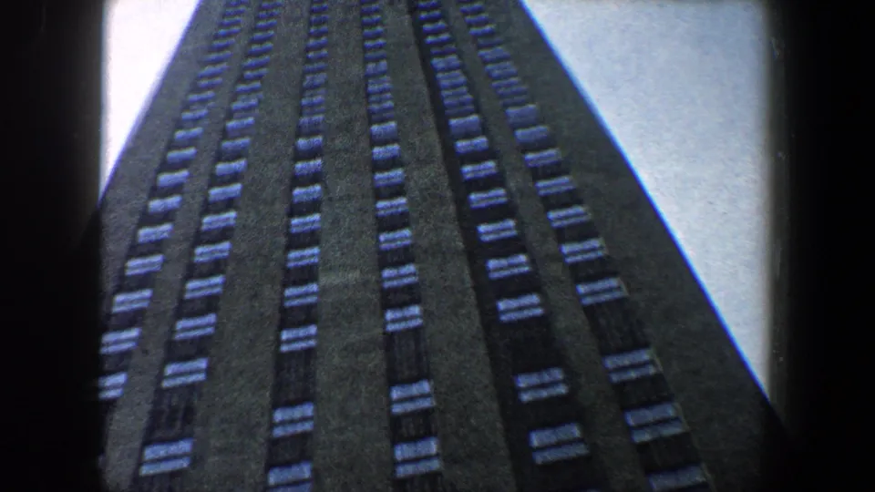 Low-angle 8mm view of a tall New York City building facade with rows of windows receding upward.