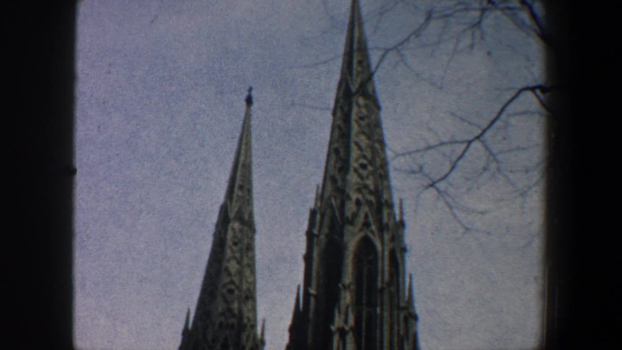 1960 New York City 8mm frame showing pointed Gothic church spires, bare branches, and pale sky from a street-level view.