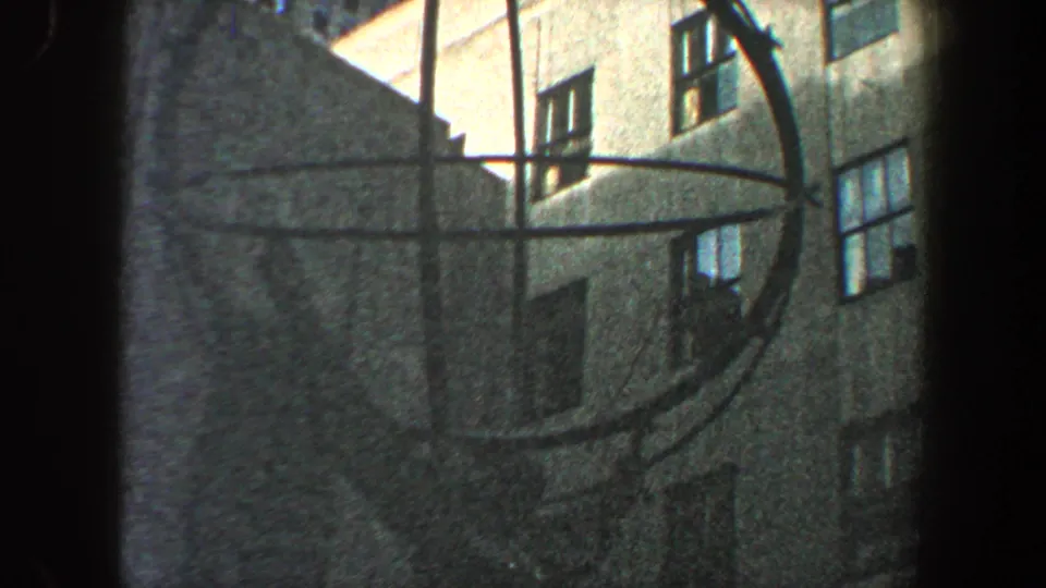 Handheld 8mm frame from New York City in 1960 showing the metal circular form against shadowed building facades.