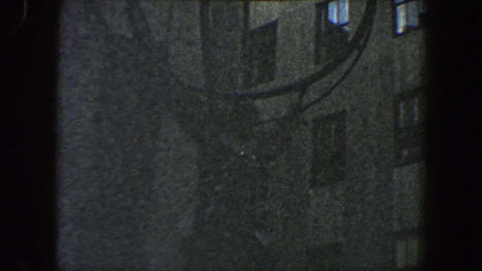 Soft, grainy 8mm frame showing the lower portion of the circular metal sculpture near tall New York City buildings.