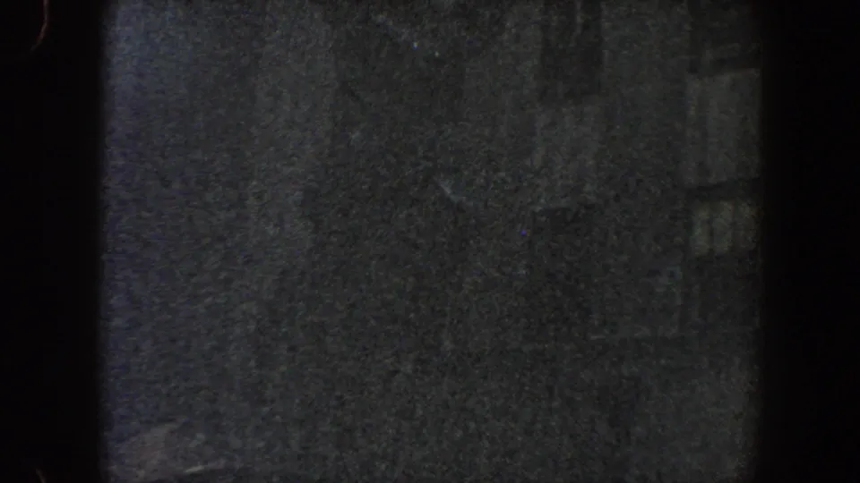 Dark final 8mm frame where the circular metal form is faintly visible beside shadowed New York City building windows.