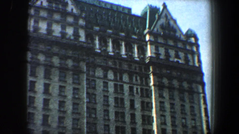 1960 New York City 8mm frame centered on the upper portion of an ornate building with gabled rooflines, window rows, and masonry detail.