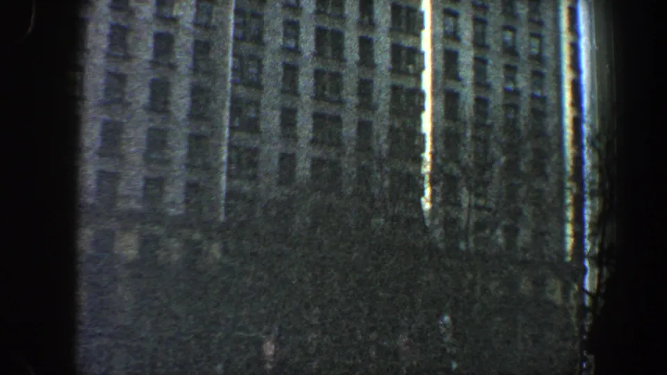 1960 New York City frame with a high-rise facade, shadowed vertical border, and darker lower tree area as the camera pans downward.