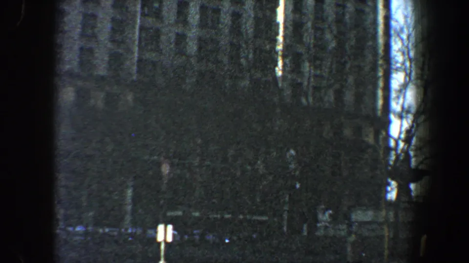 1960 New York City 8mm frame showing the lower portion of the high-rise partly hidden by bare trees and shadowed foreground.