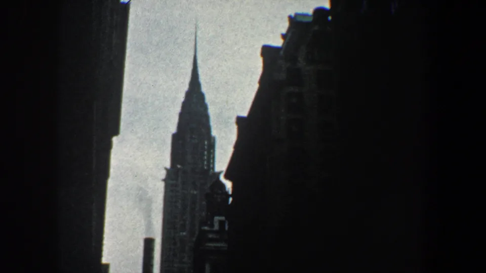 The Chrysler Building remains visible through a narrow urban opening, with dark facades and a foreground vent below.