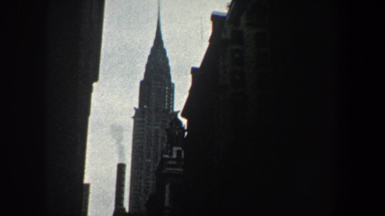 1960 New York City 8mm frame showing the Chrysler Building spire framed by dark building silhouettes and bright sky.