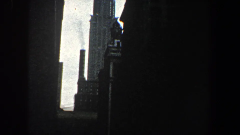 1960 New York City frame with dark vertical building forms, a partial Chrysler Building view and a smokestack near the skyline.