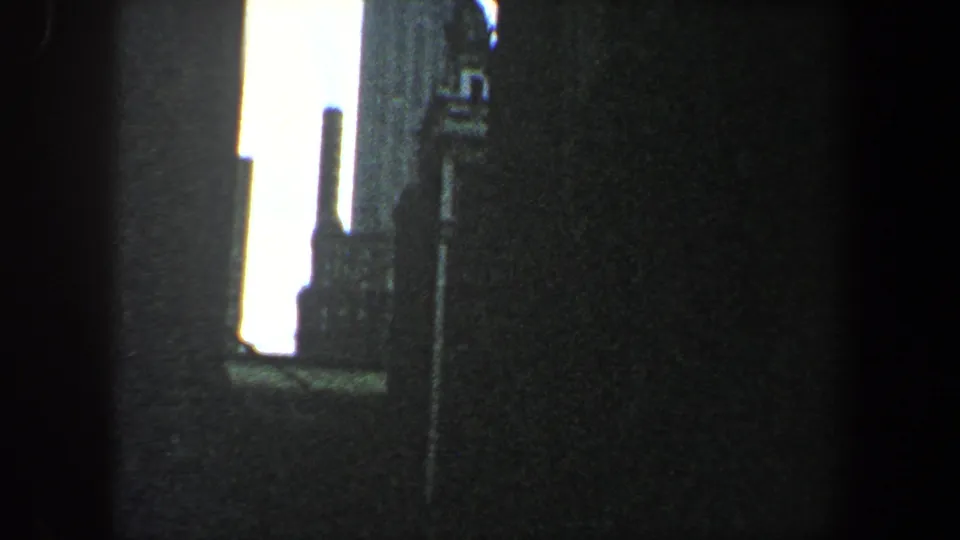 1960 New York City 8mm frame showing a narrow bright opening between dark buildings with part of the Chrysler Building visible.