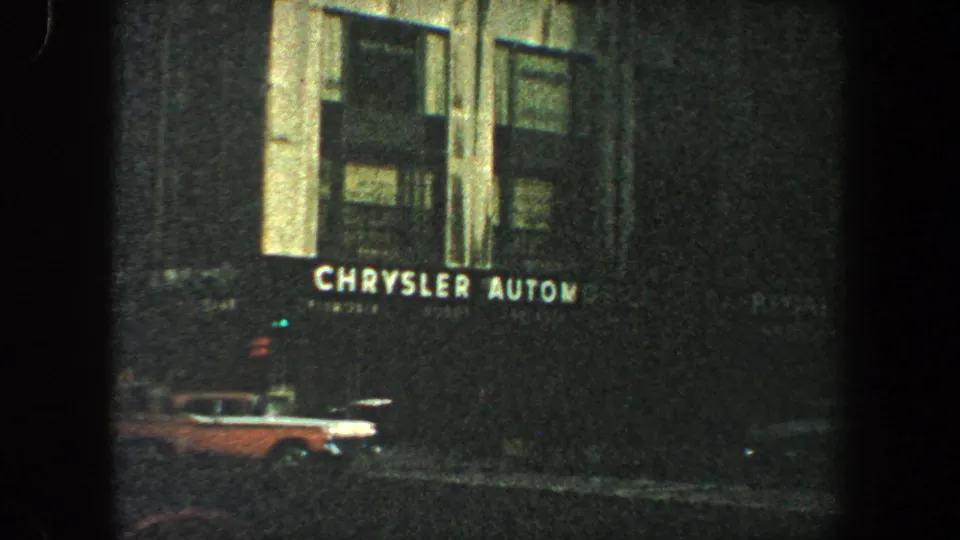 Night street view in New York City showing Chrysler Automobiles signage and a period car near the curb.